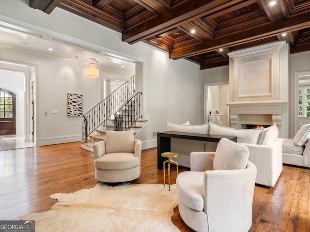 living room with a warm lit fireplace, baseboards, hardwood / wood-style flooring, stairs, and crown molding