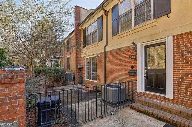 view of side of home featuring brick siding, fence, entry steps, and central AC unit