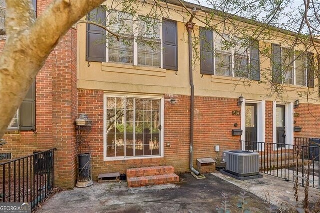 back of house with central AC unit, brick siding, a patio area, and stucco siding