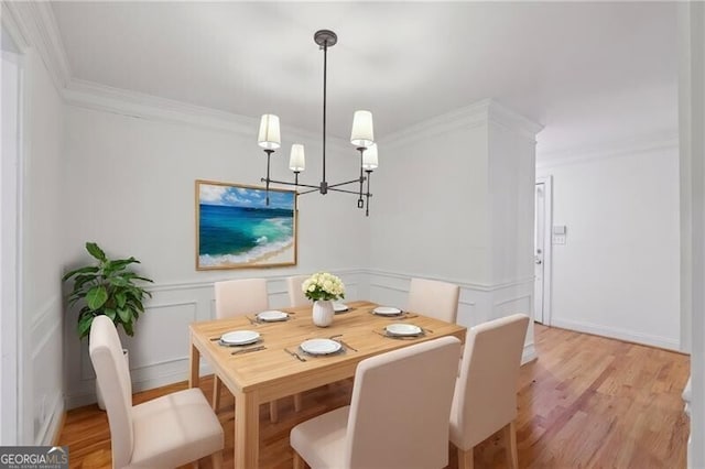 dining room featuring a chandelier, ornamental molding, light wood-style flooring, wainscoting, and a decorative wall