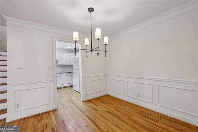 unfurnished dining area with a chandelier, ornamental molding, light wood-style flooring, stairway, and wainscoting