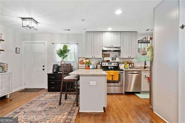 kitchen with appliances with stainless steel finishes, a kitchen breakfast bar, wood-type flooring, a kitchen island, and light stone counters