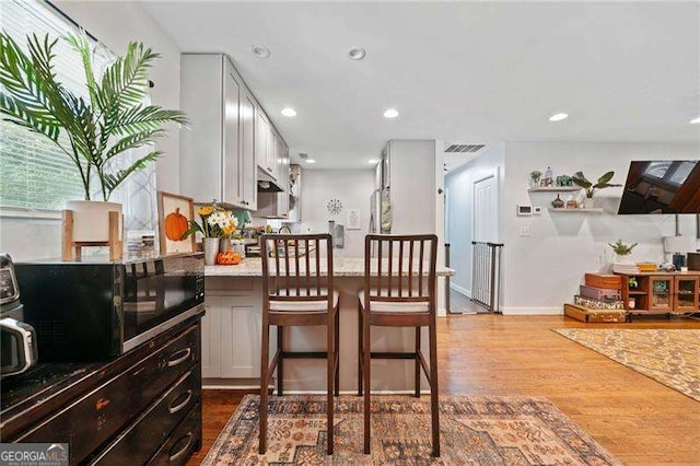 kitchen featuring white cabinetry, light stone countertops, wood-type flooring, and a breakfast bar area