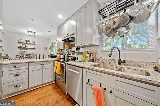 kitchen featuring sink, light wood-type flooring, light stone countertops, stainless steel appliances, and white cabinets