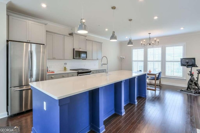 kitchen with pendant lighting, appliances with stainless steel finishes, a kitchen island with sink, and a chandelier