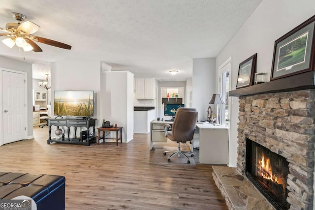 office area with a textured ceiling, a stone fireplace, wood finished floors, and a ceiling fan