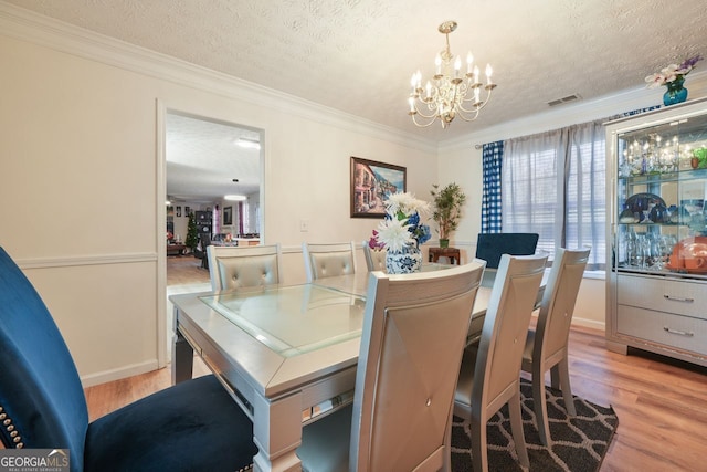 dining area with light wood-type flooring, a textured ceiling, a notable chandelier, and ornamental molding