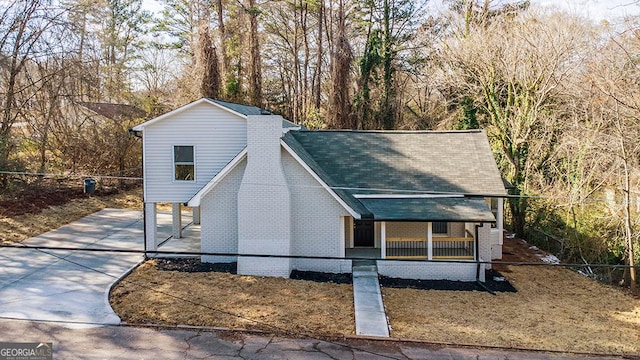 view of front facade with a shingled roof, covered porch, and brick siding