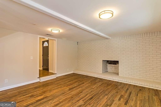 unfurnished living room with wood finished floors, brick wall, a brick fireplace, baseboards, and visible vents