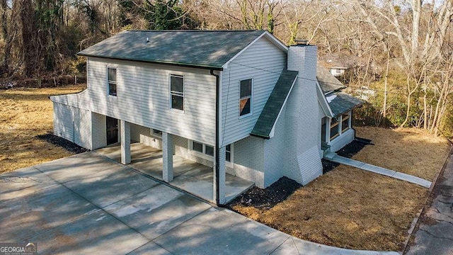 view of front of property featuring driveway, a chimney, a patio area, a shingled roof, and a forest view