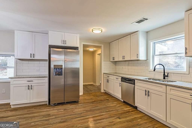 kitchen featuring white cabinetry, stainless steel appliances, dark wood-type flooring, light stone counters, and sink