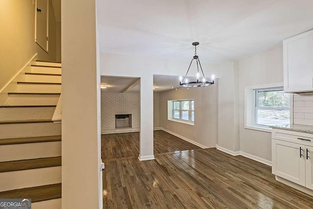 interior space featuring dark wood-type flooring, a brick fireplace, and a notable chandelier