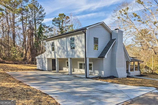 view of front facade with driveway, a chimney, a porch, and brick siding