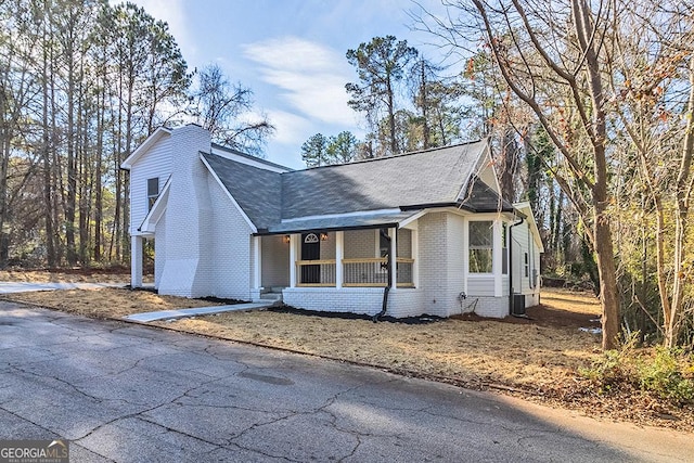 view of front of property with a porch, central AC unit, a shingled roof, and brick siding