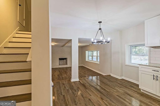 interior space featuring a brick fireplace, an inviting chandelier, wood finished floors, and baseboards