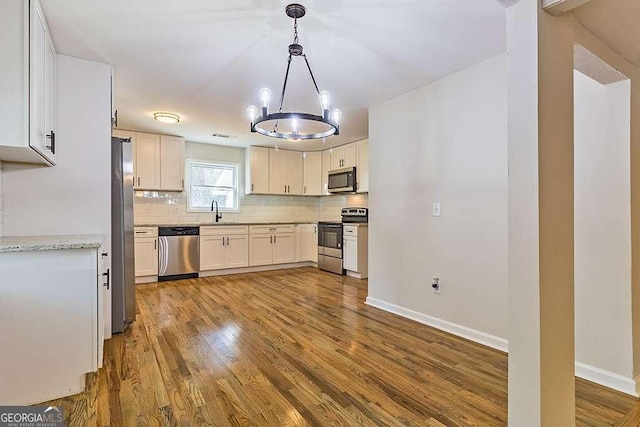 kitchen with appliances with stainless steel finishes, decorative light fixtures, white cabinetry, decorative backsplash, and light hardwood / wood-style flooring