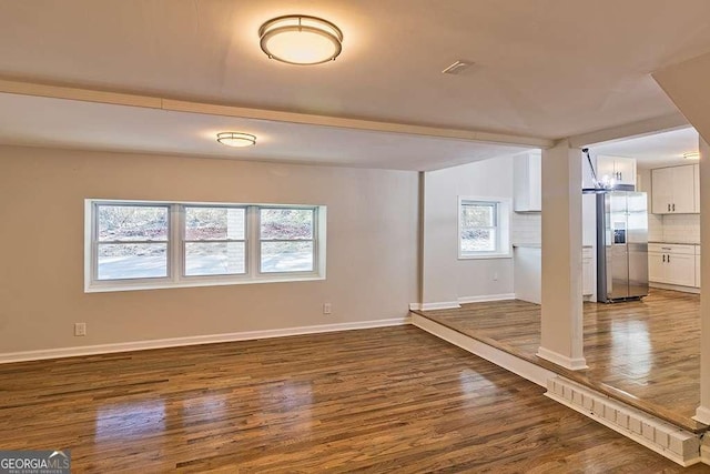 basement with baseboards, stainless steel refrigerator with ice dispenser, and dark wood-type flooring