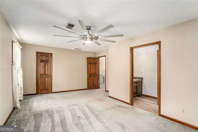 unfurnished bedroom featuring ceiling fan, light colored carpet, a textured ceiling, and connected bathroom