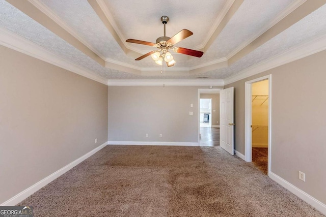 unfurnished bedroom featuring ceiling fan, a raised ceiling, a closet, a walk in closet, and crown molding