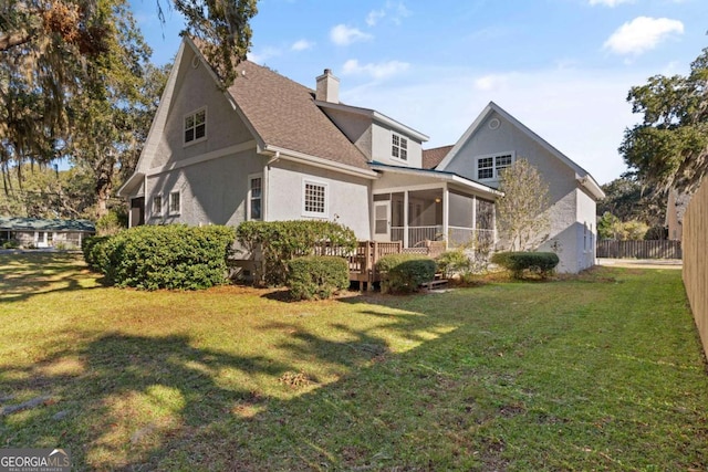 back of property featuring a deck, a yard, and a sunroom