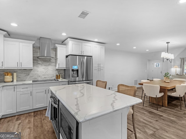 kitchen featuring appliances with stainless steel finishes, wall chimney exhaust hood, white cabinets, and hanging light fixtures