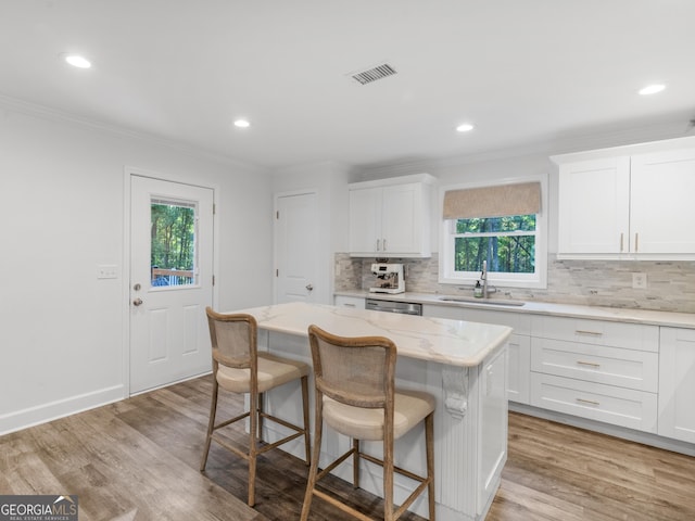 kitchen with a kitchen island, sink, light hardwood / wood-style flooring, light stone countertops, and white cabinets