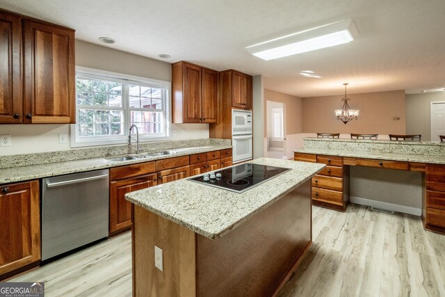 kitchen with black electric stovetop, light stone counters, hanging light fixtures, and sink