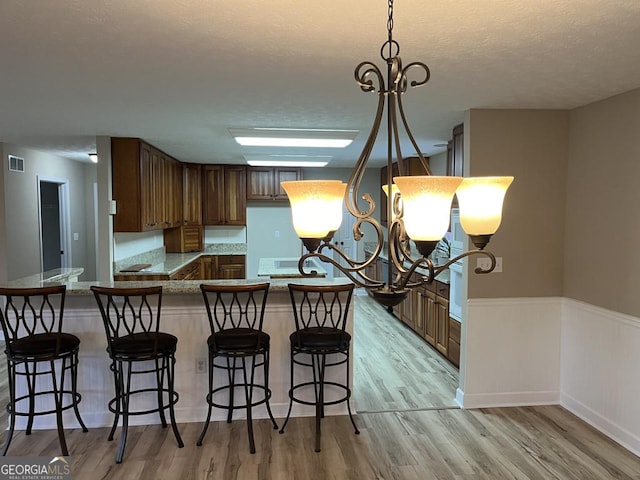 kitchen featuring kitchen peninsula, light wood-type flooring, hanging light fixtures, a chandelier, and light stone counters