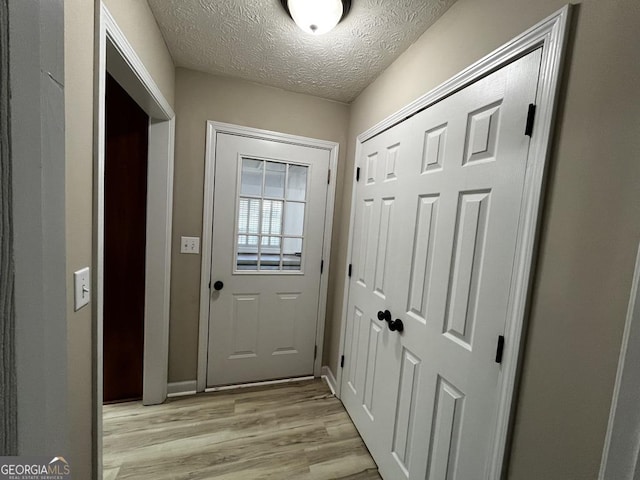 doorway to outside with a textured ceiling and light hardwood / wood-style flooring