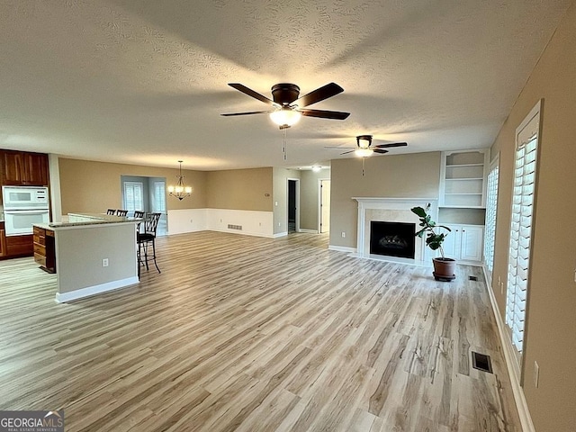 unfurnished living room featuring a textured ceiling, light hardwood / wood-style floors, ceiling fan with notable chandelier, and built in shelves