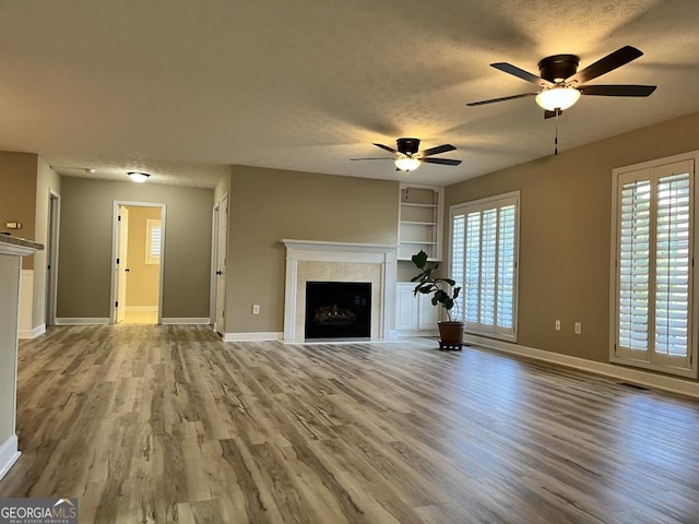 unfurnished living room with ceiling fan, built in shelves, a textured ceiling, and light hardwood / wood-style flooring