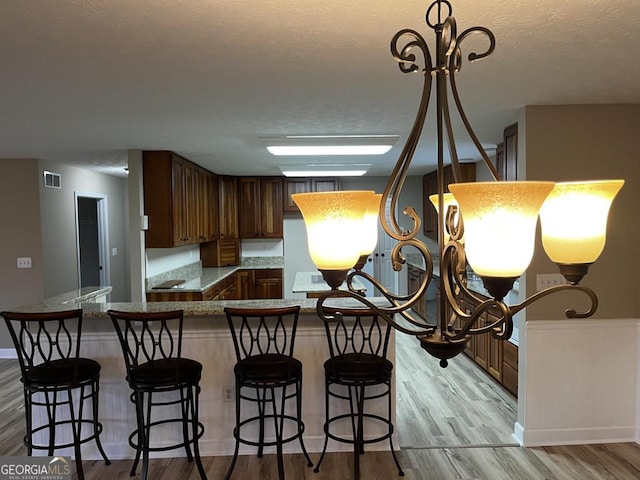 kitchen with an inviting chandelier, light hardwood / wood-style floors, kitchen peninsula, and a breakfast bar