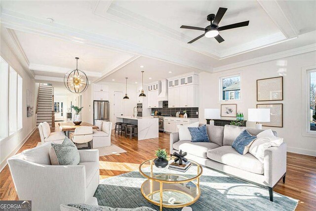 living room with light hardwood / wood-style floors, ceiling fan with notable chandelier, and ornamental molding