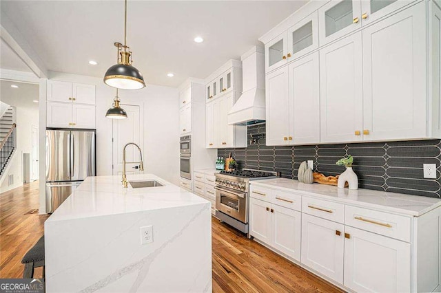 kitchen with appliances with stainless steel finishes, premium range hood, white cabinetry, pendant lighting, and a sink