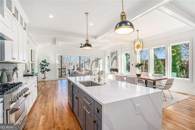 kitchen with decorative light fixtures, appliances with stainless steel finishes, open floor plan, white cabinets, and a sink