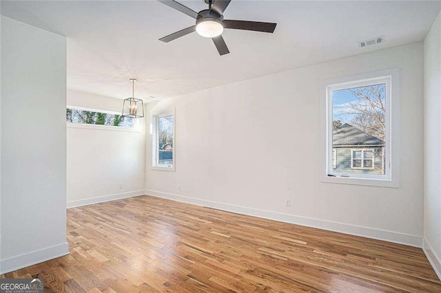 unfurnished room with a ceiling fan, visible vents, baseboards, and wood finished floors