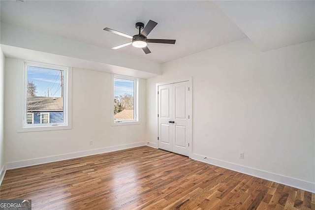 unfurnished bedroom featuring ceiling fan, baseboards, dark wood finished floors, and a closet