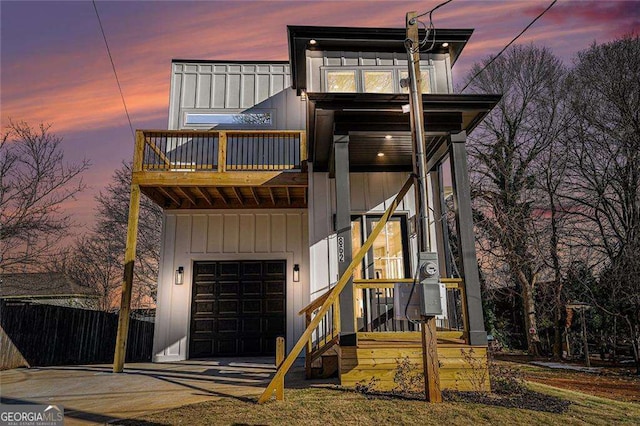 contemporary house featuring an attached garage, a balcony, fence, driveway, and board and batten siding