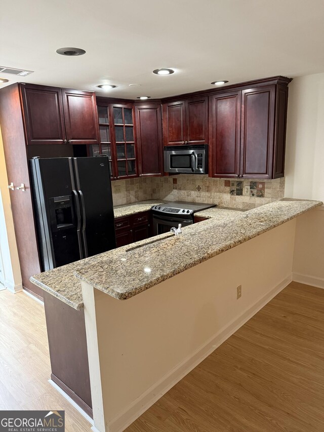 kitchen with light tile patterned floors, kitchen peninsula, appliances with stainless steel finishes, decorative backsplash, and light stone counters