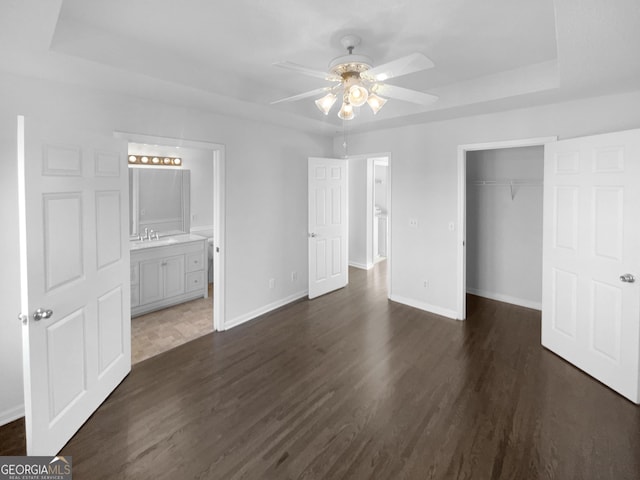 unfurnished bedroom featuring ceiling fan, a raised ceiling, sink, connected bathroom, and a closet