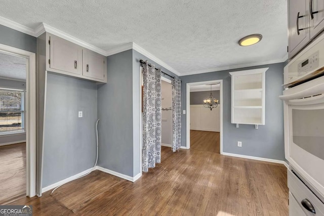 kitchen with pendant lighting, wood-type flooring, ornamental molding, a chandelier, and oven