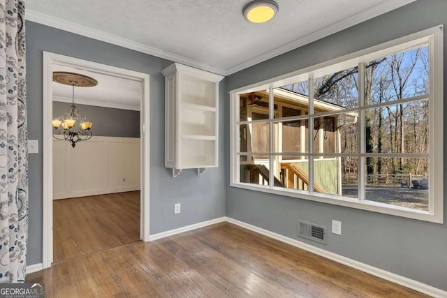 empty room featuring crown molding, an inviting chandelier, a textured ceiling, and hardwood / wood-style floors