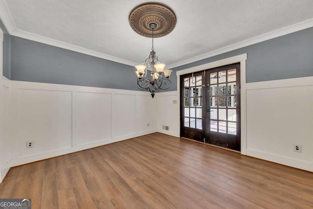 spare room with ornamental molding, wood-type flooring, french doors, and a notable chandelier