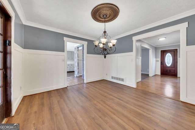 unfurnished dining area featuring hardwood / wood-style flooring, ornamental molding, and a chandelier