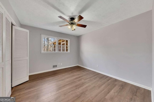 unfurnished bedroom with ceiling fan, a closet, a textured ceiling, and hardwood / wood-style flooring