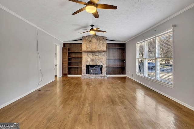 unfurnished living room featuring ceiling fan, a wood stove, lofted ceiling, built in features, and a textured ceiling