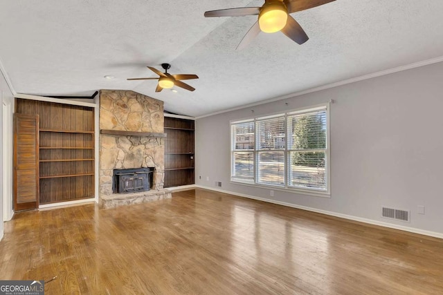 unfurnished living room featuring vaulted ceiling, crown molding, a textured ceiling, and a wood stove