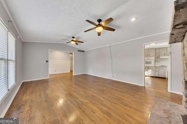 unfurnished living room featuring ceiling fan, vaulted ceiling, light wood-type flooring, ornamental molding, and a textured ceiling