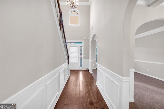 hall with an inviting chandelier, dark wood-type flooring, and ornamental molding