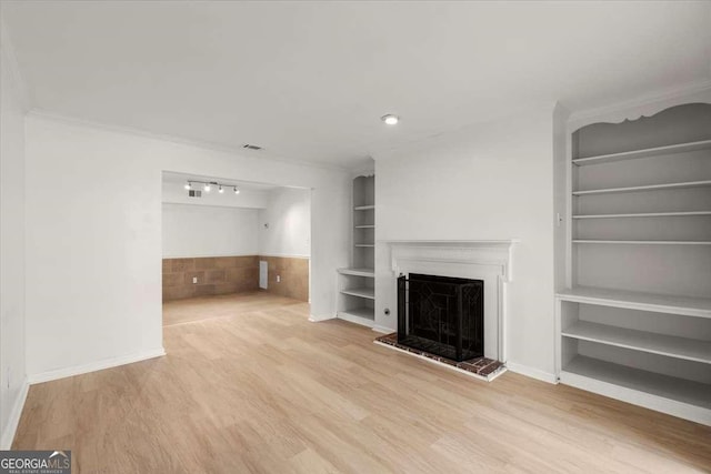 unfurnished living room featuring wood-type flooring, ornamental molding, and built in shelves